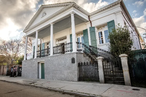 Exterior view of a white historic raised center hall villa with columns, green shutters, and an iron staircase.