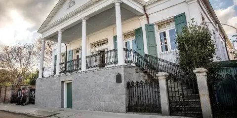 Exterior view of a white historic raised center hall villa with columns, green shutters, and an iron staircase.