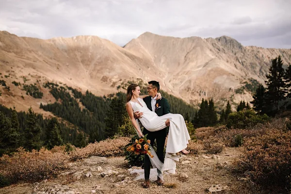 A bride and groom posing on a mountain ridge with a scenic backdrop.