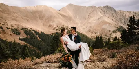 A bride and groom posing on a mountain ridge with a scenic backdrop.