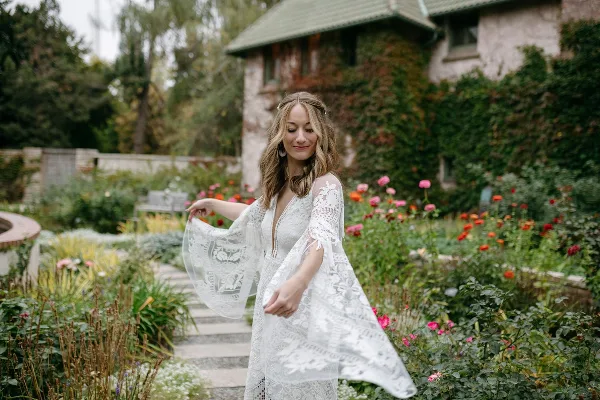 A bride with styled hair and makeup wearing a white lace dress in a garden setting.