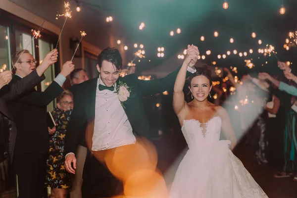 A bride and groom smiling and holding hands while walking through a sparkler tunnel at a wedding reception.