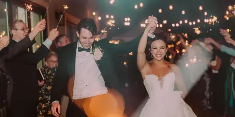 A bride and groom smiling and holding hands while walking through a sparkler tunnel at a wedding reception.