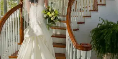 A bride in a white gown and veil walks down a wooden staircase toward a groom in a grey suit.