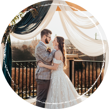 A bride and groom embracing under a fabric-draped wedding arbor overlooking a blueberry field.