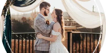 A bride and groom embracing under a fabric-draped wedding arbor overlooking a blueberry field.