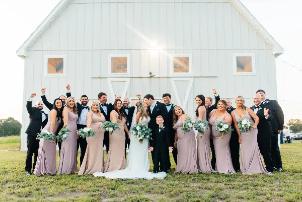 A wedding party posing in front of a white barn venue