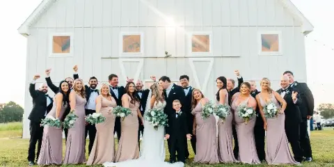 A wedding party posing in front of a white barn venue