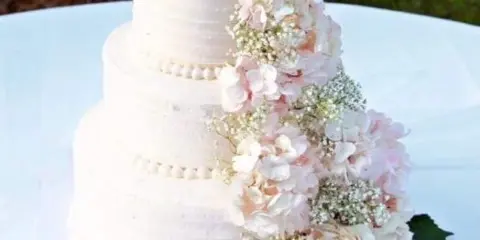 A three-tiered white wedding cake decorated with pink and white flowers and a gold topper.