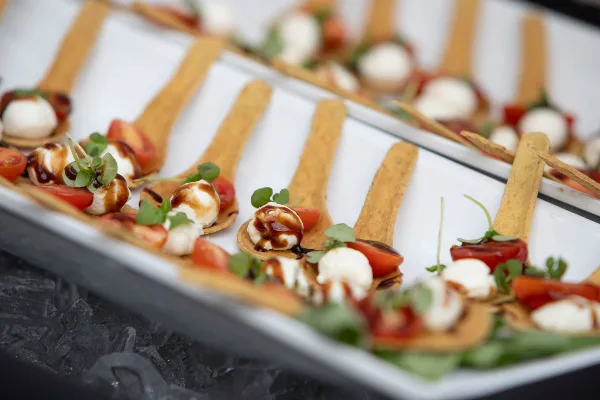 A close-up of a catering buffet featuring rows of appetizers served on wooden spoons, garnished with fresh herbs and balsamic glaze.
