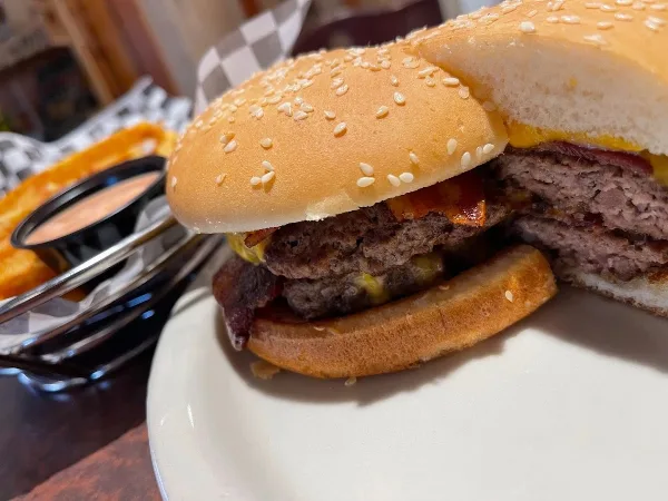 A close-up of a double bacon cheeseburger on a sesame seed bun served with french fries.