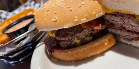 A close-up of a double bacon cheeseburger on a sesame seed bun served with french fries.