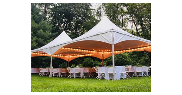 A white high-peak tent set up on a grassy lawn with string lights, tables, and chairs arranged for an event.