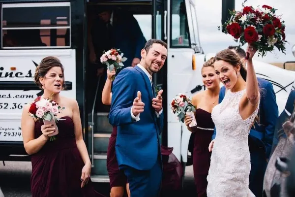 A bride, groom, and wedding party boarding a white party bus.