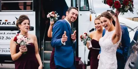A bride, groom, and wedding party boarding a white party bus.
