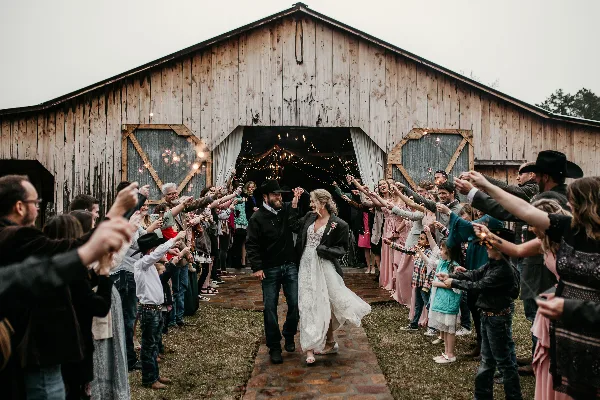 A bride and groom walking through a line of guests holding sparklers outside a wooden barn.
