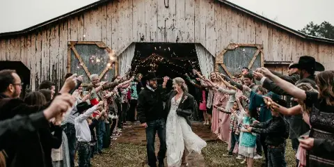 A bride and groom walking through a line of guests holding sparklers outside a wooden barn.