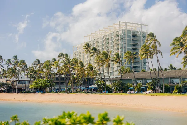 Exterior view of a luxury beachfront resort with a large building, palm trees, and a swimming pool.