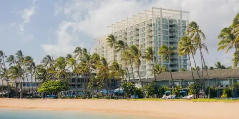 Exterior view of a luxury beachfront resort with a large building, palm trees, and a swimming pool.