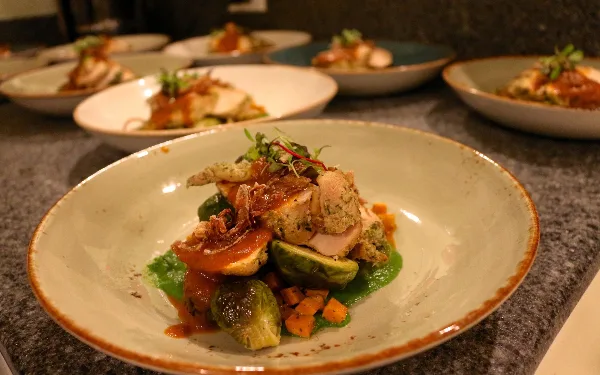 A plated dish featuring chicken, brussels sprouts, and a red sauce served in a ceramic bowl.