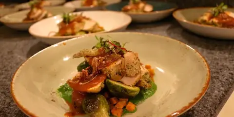 A plated dish featuring chicken, brussels sprouts, and a red sauce served in a ceramic bowl.