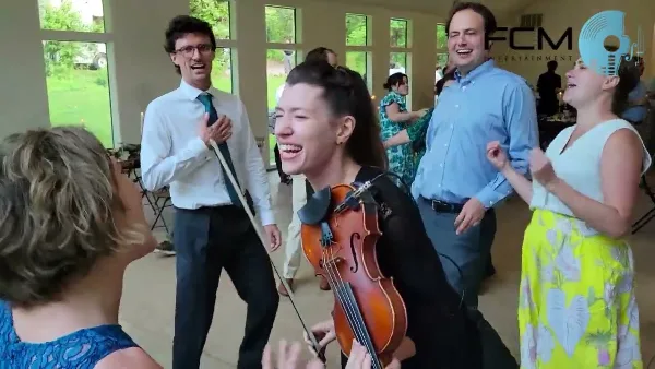 A musician playing a violin while dancing with guests at a wedding reception.