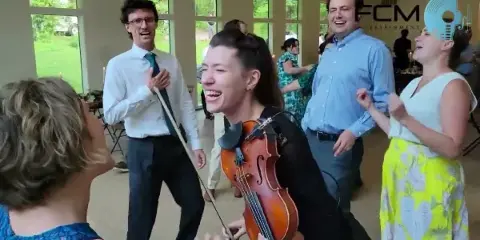 A musician playing a violin while dancing with guests at a wedding reception.
