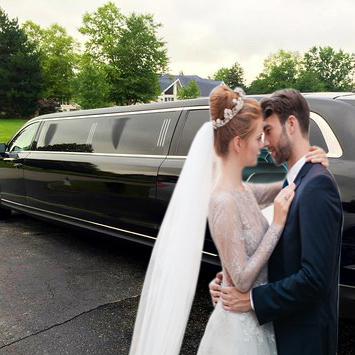A bride and groom embracing in front of a black stretch limousine.