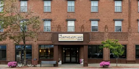 Exterior view of The Northeastland Hotel, a multi-story red brick building with a central entrance and signage.