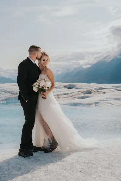 Bride and groom standing together on an Alaskan glacier, with the bride holding a bouquet.