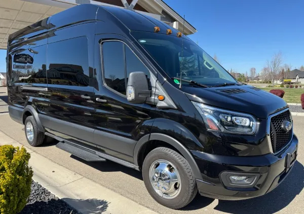 A black Ford Transit passenger van parked on a driveway in front of a residential building.