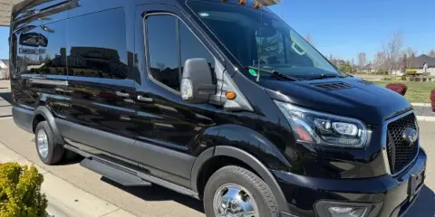 A black Ford Transit passenger van parked on a driveway in front of a residential building.