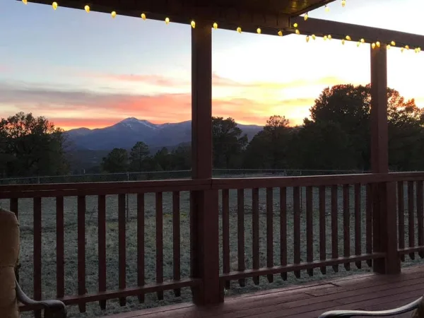 Covered wooden porch with string lights overlooking a field and mountains at sunset
