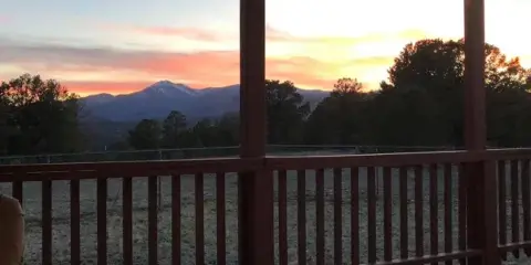 Covered wooden porch with string lights overlooking a field and mountains at sunset