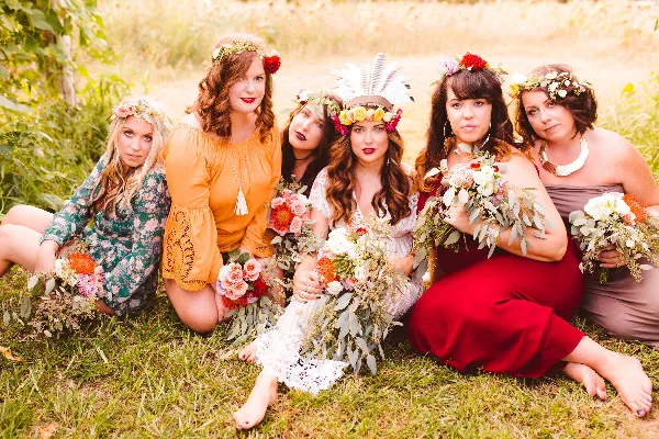 A group of women wearing floral crowns and holding bouquets in a grassy field.
