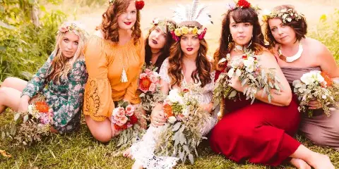 A group of women wearing floral crowns and holding bouquets in a grassy field.