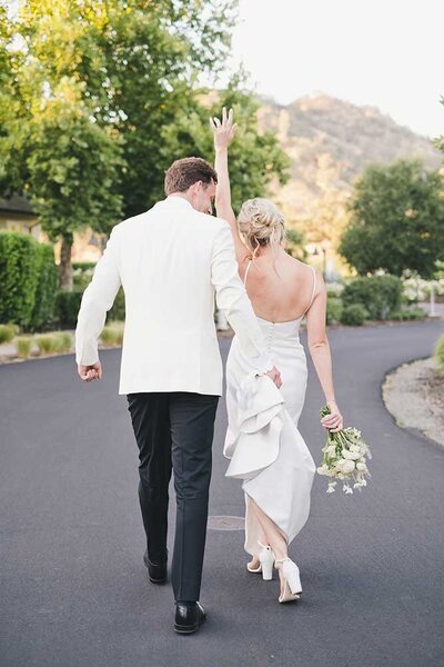 A bride and groom walking away from the camera on a paved path with a mountain in the background.