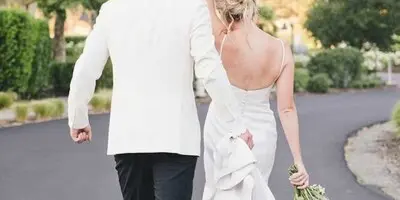 A bride and groom walking away from the camera on a paved path with a mountain in the background.