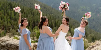 A bride and four bridesmaids in blue dresses holding bouquets, posing on a rocky mountain overlook.
