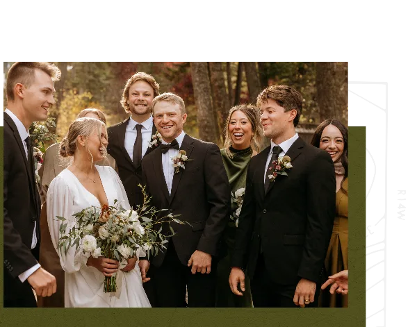A wedding party including the bride and groom posing together outdoors in a wooded area.
