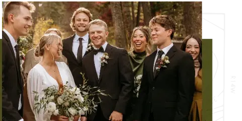 A wedding party including the bride and groom posing together outdoors in a wooded area.