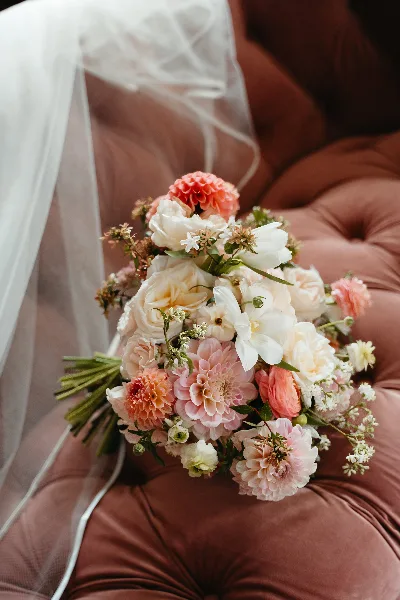 A close-up of a wedding bouquet with pink and white flowers resting on a tufted velvet surface.