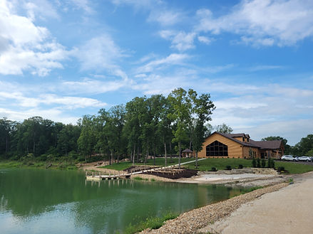 A rustic log cabin event center located on the shore of a lake with a dock and surrounding trees.