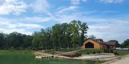 A rustic log cabin event center located on the shore of a lake with a dock and surrounding trees.
