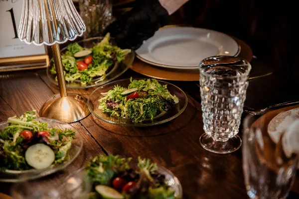 A close-up of a plated salad with greens, tomatoes, and cucumbers on a wooden table, accompanied by glassware and a table number.