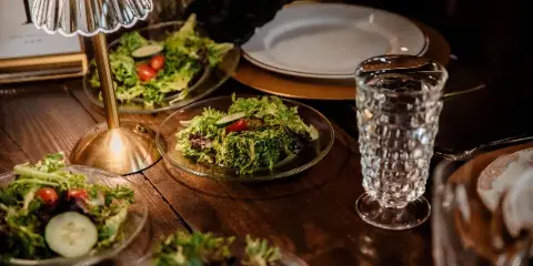 A close-up of a plated salad with greens, tomatoes, and cucumbers on a wooden table, accompanied by glassware and a table number.