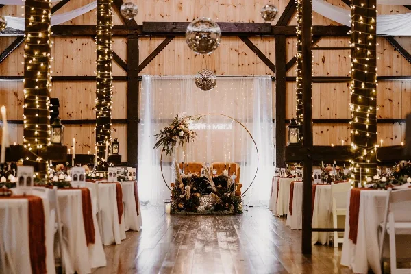 Interior of a rustic wooden barn wedding venue with a dance floor, reception tables, and a decorated head table.