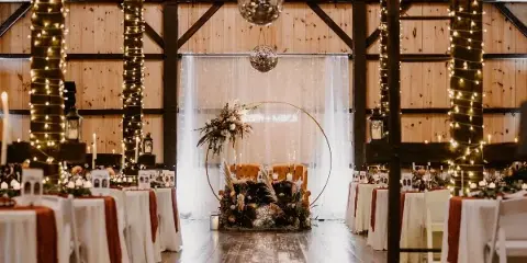 Interior of a rustic wooden barn wedding venue with a dance floor, reception tables, and a decorated head table.