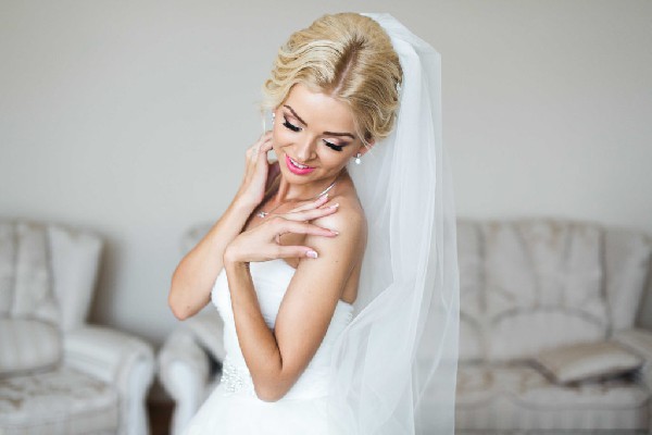 A bride with an elegant updo hairstyle and makeup, wearing a white dress and veil.