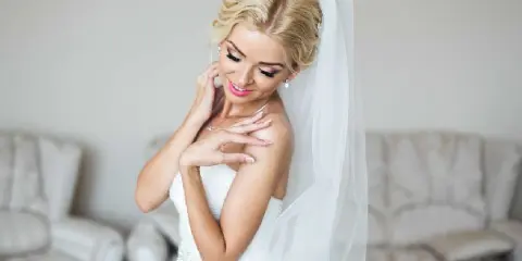 A bride with an elegant updo hairstyle and makeup, wearing a white dress and veil.